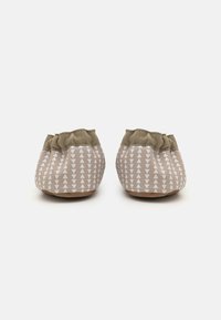 Myke beige tøfler med et strukturert mønster av hvite trekanter, elastisk topp og en lysebrun såle. Lettvekts- og koselig design.