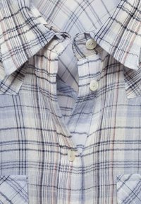 Camisa de cuadros azul claro con botones, cuello, dos bolsillos y botones blancos. La tela parece suave con un acabado ligeramente texturizado.