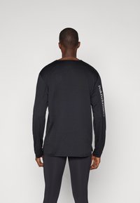 Sort langærmet skjorte med en afslappet pasform, der har en rund hals og logo langs venstre ærme. Stoffet ser glat og let ud.
