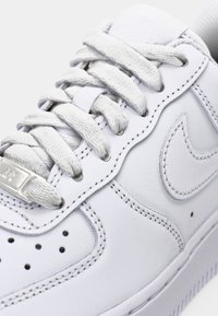 Close-up of white leather sneaker with textured laces, perforations near toe, and stitched Nike swoosh logo on the side.