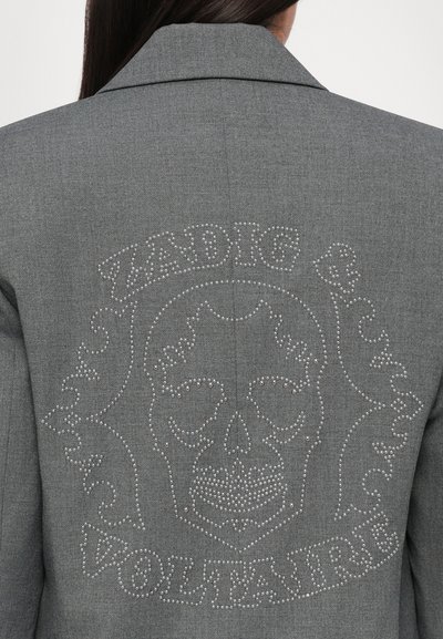 Šedý blazer s přizpůsobeným designem. Na zadní straně se nachází grafika lebky s krystaly a text "ZADIG & VOLTAIRE". Hladká textura, strukturovaný tvar.
