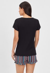 Black short-sleeve top with frilled edges, paired with striped shorts in red, blue, and white, featuring a ruffled hem. Back view.