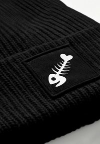 Black knit beanie with a textured pattern, featuring a square black patch. The patch displays a white fishbone graphic.