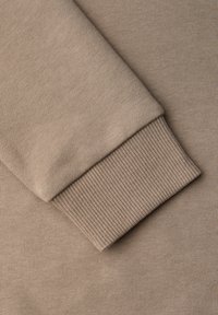 Tissu beige à texture lisse, doté d'un poignet côtelé. Le poignet présente un motif tricoté contrastant, renforçant le détail structurel.