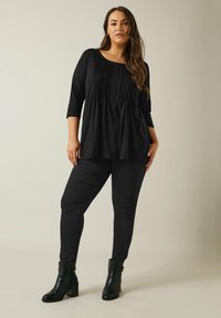 Zwarte tuniek met driekwart mouwen, voorzien van verticale plooien, gecombineerd met zwarte skinny jeans en enkelboots. Glad materiaal overal.