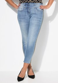 Jeans ajustados de mezclilla azul claro, con un diseño ceñido, detalles de franjas laterales en tono dorado y estilo clásico de cinco bolsillos.