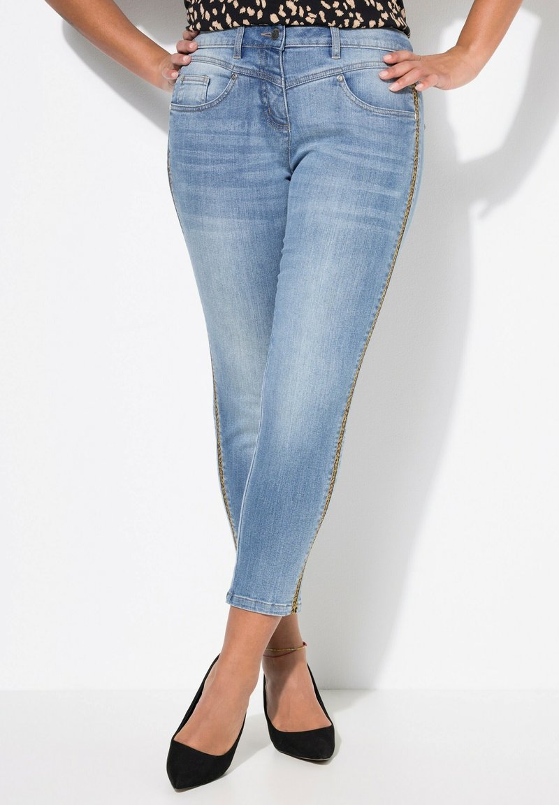 Jeans ajustados de mezclilla azul claro, con un diseño ceñido, detalles de franjas laterales en tono dorado y estilo clásico de cinco bolsillos.