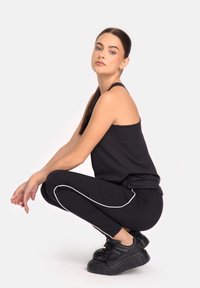 Must kollane ilma varrukatop ja mustad sportleggarid, millel on valged küljeribad. Mudel kannab massiivseid musti spordijalgu. Sile kangast tekstuur.