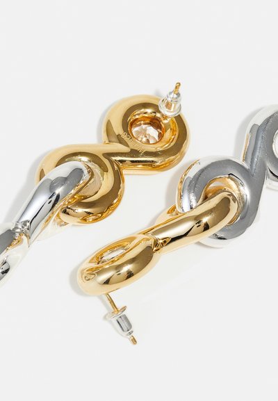 Gold- und Silberohrringe mit verschlungenen Gliedern, glatten Oberflächen und einem kleinen klaren Edelsteindetail im goldenen Glied.