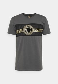 Šedé tričko s krátkým rukávem, které má černý vodorovný pruh se zlatým řeckým motivem a logem uprostřed. Vyrobeno z měkké tkaniny.