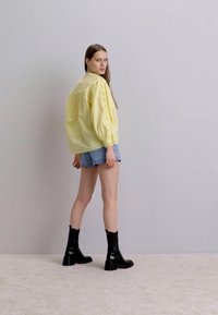 Blouse jaune à manches longues avec des manches bouffantes et des broderies, associée à un short en denim bleu clair et des bottines noires.