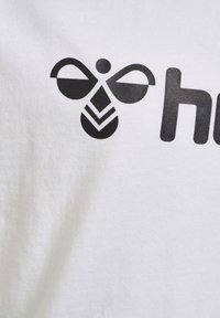 Hvid t-shirt stof med et sort grafisk design af et stiliseret bi-symbol med rundede vinger og et geometrisk krop mønster.