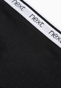 Juodas audinys su balta elastinga juosta, ant kurios pakartotinai užrašyta "next". Minkšta tekstūra, prigludęs dizainas ir vienoda spalva.