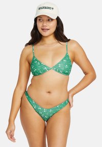 Grön bikini med blommönster, som har en triangelbehå med tunna remmar och en låg midja på bikiniunderdelen, bägge i slät tyg.