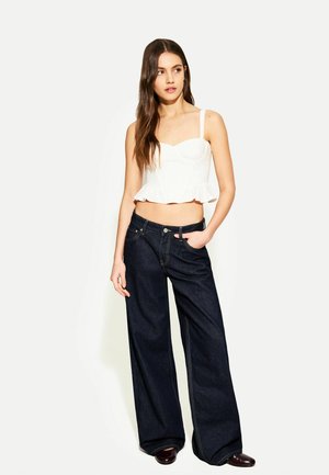 Top crop bianco con peplum e spalline sottili abbinato a pantaloni larghi in denim scuro a vita alta con cuciture a contrasto e tasche frontali.