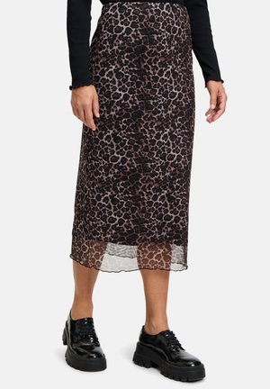 Kvinde iført en brun og sort midi-nederdel med leopardprint og transparent kant, sort langærmet top og sorte chunky platform sko.