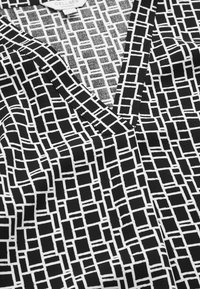 Schwarzes und weißes gemustertes Gewebe mit einem geometrischen Design, das verschiedene rechteckige Formen zeigt. V-Ausschnitt, glatte Textur.