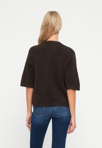 Mörkbrun, kortärmad tröja med avslappnad passform, ribbad krage och mjuk textur, tillsammans med fitted blå jeans med ett sydd mönster.
