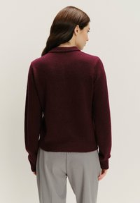 Burgundský pletený svetr s dlouhými rukávy, žebrovanými manžetami a lemem, s měkkou texturou a klasickým designem límce.