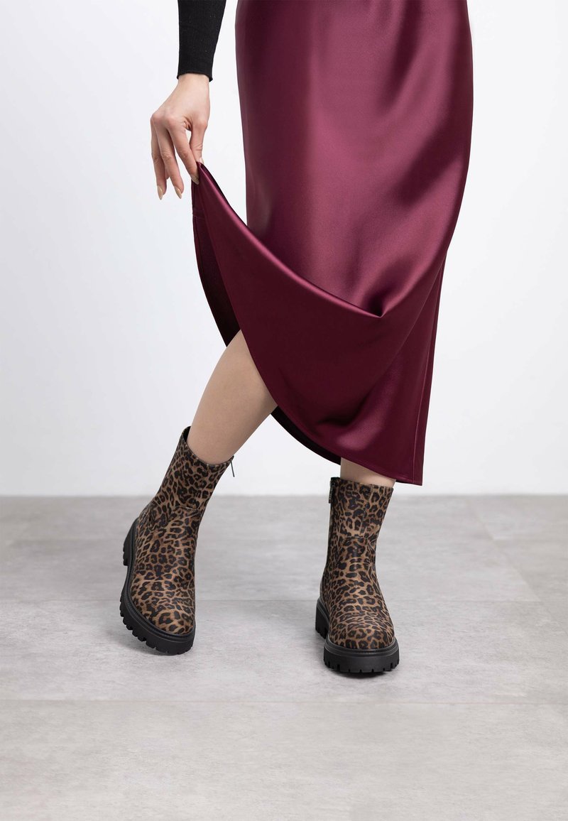 Botas de tobillo con estampado de leopardo y una superficie texturizada, suelas de goma negras y un diseño de altura media, combinadas con una falda de satén burdeos brillante.
