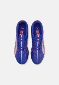 Zapatillas deportivas moradas con acentos rosas, parte superior texturizada, diseño elegante y cierre de cordones. Presenta un logo en la lengüeta y en el costado.