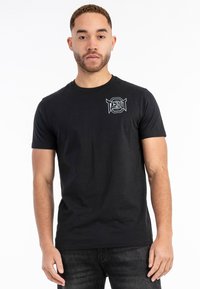 Must värvi puuvillane T-särk, millel on valge prinditud "TAPOUT" logo, ümar kaelus, lühikesed varrukad ja tavaline lõige.