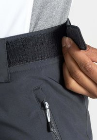 Schwarze Hose mit einem strukturierten Bund und einem Klettverschluss. Eine Reißverschlusstasche mit einem kontrastierenden Zugband ist ebenfalls sichtbar.