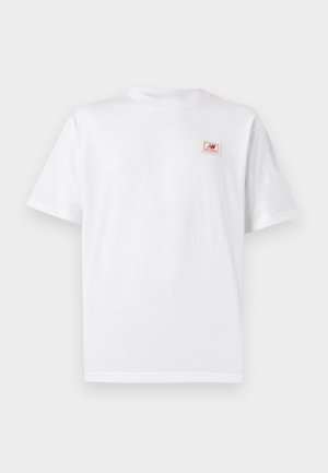 Osoba s vrkočmi, ktorá má na sebe biele tričko s červeným logom "NB new balance" na chrbte a olivovo zelené nohavice cargo, otočená chrbtom.