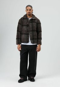 Fuzzy brown and black checkered jacket with a button front and collar, paired with black wide-leg pants and black shoes.