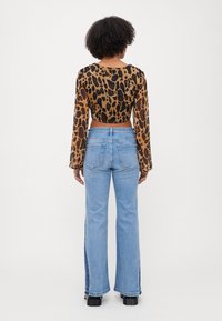 Kuttet, langermet topp laget av gjennomsiktig, leopardmønstret stoff; kombinert med høytlivde, lys blå svalejeans og svarte platåstøvler.