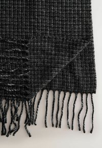 Zwarte en grijze gewoven sjaal met een geruit patroon, voorzien van franjes en een zachte textuur. Rechthoekige vorm met een warme uitstraling.