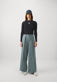 Top preto com riscas e mangas longas, adornado com um logo prateado, combinado com calças de ganga largas em azul claro e ténis brancos, complementado com um boné azul marinho.