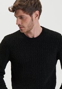 Maglione nero con texture, caratterizzato da un motivo a coste, collo rotondo e maniche lunghe. Il tessuto appare morbido e caldo.