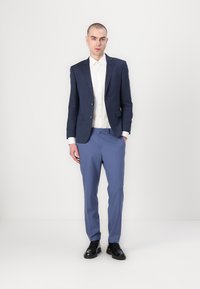 Navy blazer with textured fabric, white shirt, light blue trousers, and black shoes. Straight-cut pants and fitted cut blazer.