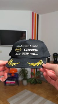 Must kork, millel on tikitud kollane laureli kujundus, millel on mitu logo ja tekst: "Build, Destroy, Rebuild," Greddy, huf ja KG21.