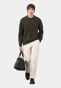 Ciemnozielony sweter z dekoltem, trzema guzikami, w połączeniu z kremowymi spodniami i czarną skórzaną torebką. Czarne buty.