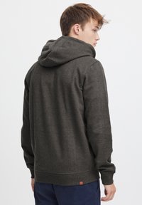 Sudadera con capucha de color gris oscuro, con puños y dobladillo acanalados, textura suave y una pequeña etiqueta de marca en la parte inferior de la espalda.