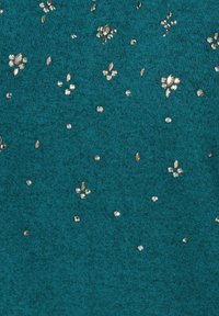 Pull en tricot turquoise orné de sequins métalliques dispersés en formes florales, créant une finition texturée et décorative sur le tissu.