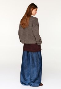 Bruine cropped trui, lange bordeauxrode top en wijde blauwe spijkerbroek. Gestructureerde gebreide stof, ontspannen silhouet met zichtbare stiksels.