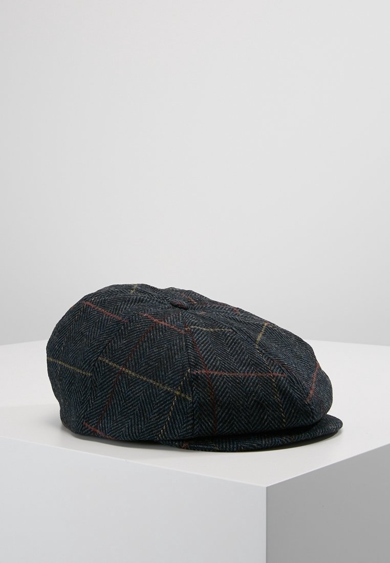 Casquette plate en tweed gris foncé avec un motif à carreaux rouge et jaune subtil, reposant sur une surface blanche sur un fond uni.