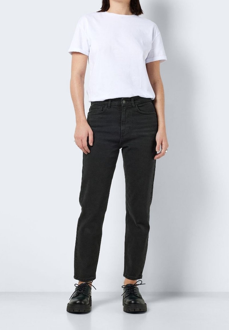 Jean noir taille haute avec une coupe droite, associé à un t-shirt blanc uni et des chaussures à lacets noires.