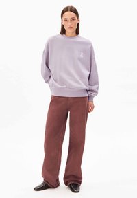 Sweat-shirt lavande avec un col rond et des poignets côtelés, assorti à un pantalon large bordeaux et des chaussures noires à bouts pointus ornées de clous.