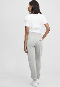 Ljusgrå sweatpants med smal passform, elastisk midja och en bakficka. Bärs med en enkel vit t-shirt med kort ärm.