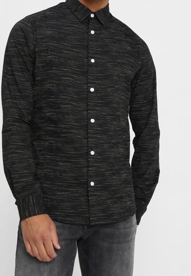 Camicia nera a maniche lunghe con motivo strutturato in grigio scuro, dotata di chiusura frontale con bottoni bianchi e colletto. Indossata con jeans grigi.