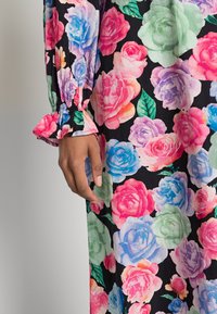 Vestido floral com fundo preto, apresentando grandes rosas em tons de rosa, azul e verde. Mangas elásticas e franzidas adicionam textura e detalhe.