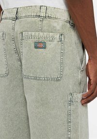 Světle zelené denimy s viditelným švem, mnoha kapsami a modro-červeným logem Dickies na zadní kapse.