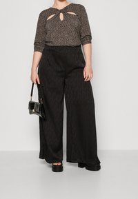 Pantaloni neri a gamba larga abbinati a una maglietta con stampa leopardata e dettaglio a oblò. Gli accessori includono una piccola borsa nera. Trame lisce.