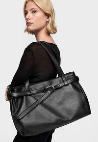 Czarna skórzana torba typu tote o solidnej konstrukcji, płaskich rączkach i subtelnie fakturowanym wykończeniu. Posiada ozdobny pasek z metalowymi akcentami.