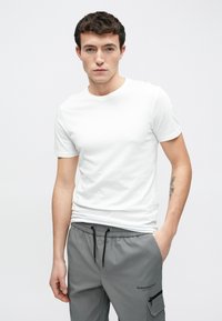 Fehér, kerek nyakkivágású rövid ujjú póló, szürke, elasztikus derékpántos nadrággal, fekete húzózsinórokkal és zsebekkel párosítva.