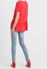 Punainen peplum-toppi lyhyillä hihoilla, valmistettu pehmeästä kankaasta. Yhdistetty vaaleansinisiin skinny-farkkuihin ja punaisiin korokepolkimiin.